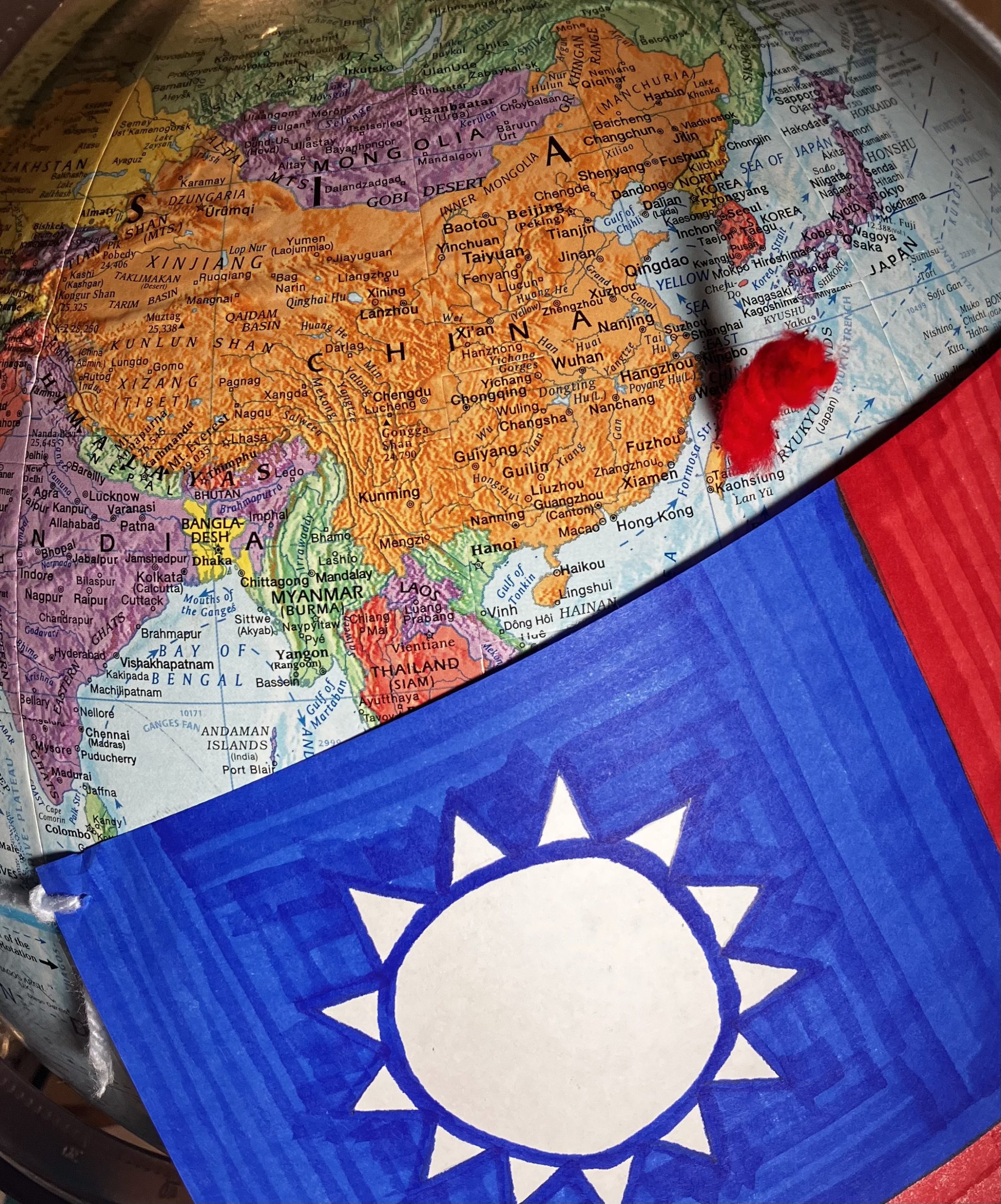 Taiwanese flag draped over globe showing China and Taiwan. Taiwan is marked with a needle covered in red yarn.